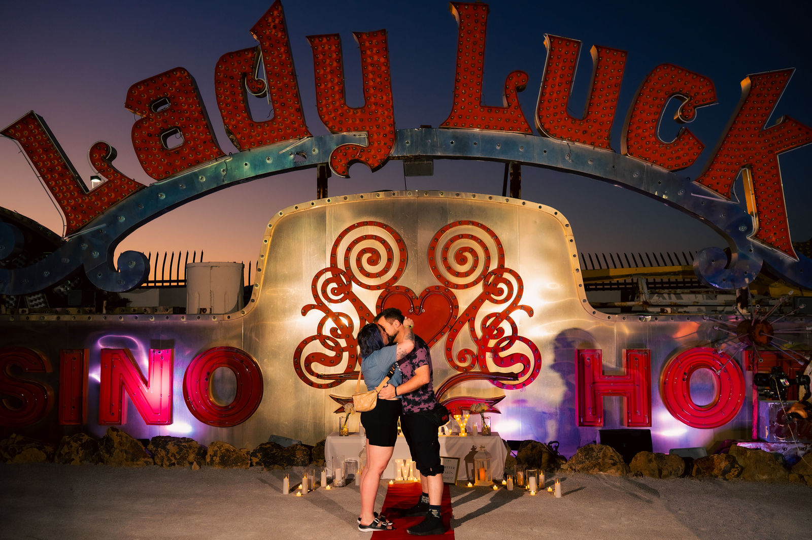 Romantic marriage proposal planned by KayC Events at the Neon Museum in Las Vegas, with a candlelit red carpet aisle beneath the Lady Luck sign at dusk