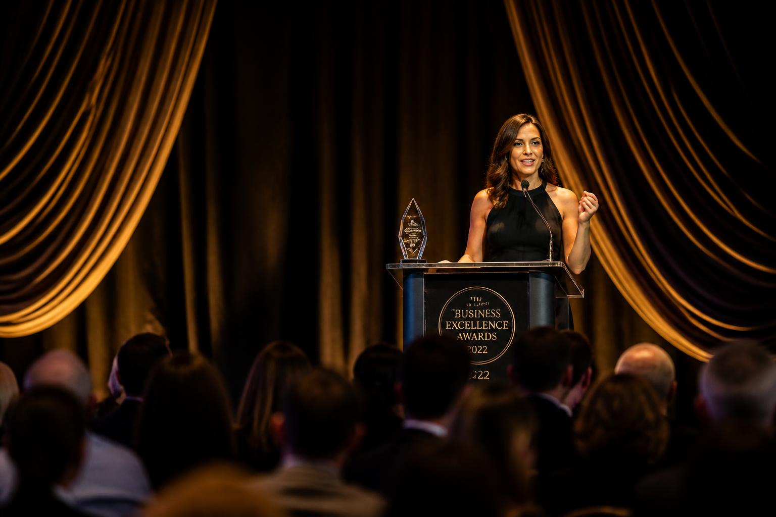 A single presenter stands on a draped stage holding a crystal award during an annual corporate recognition gala dinner.